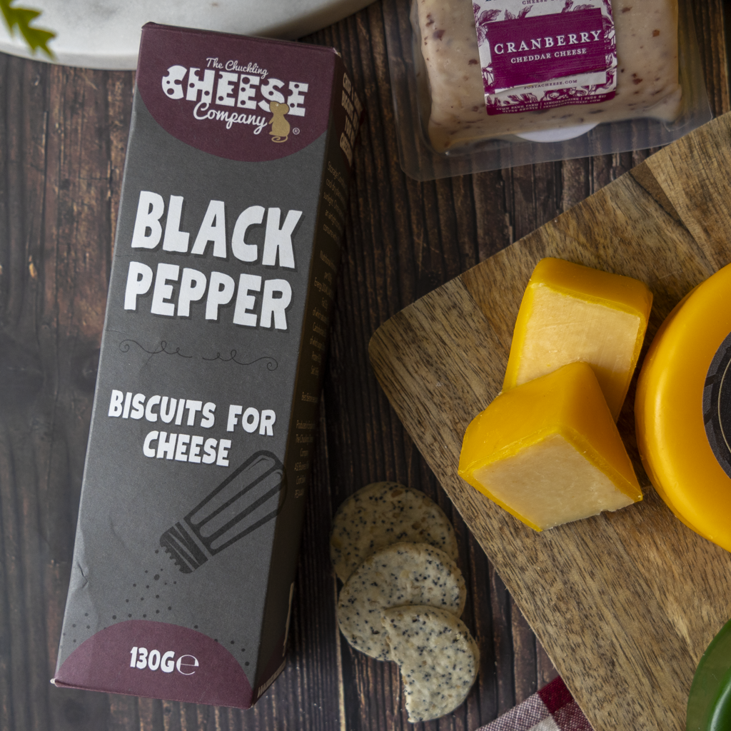 Black Pepper biscuits with Cranberry Cheddar, cheese cubes and crackers on a wooden cheeseboard.