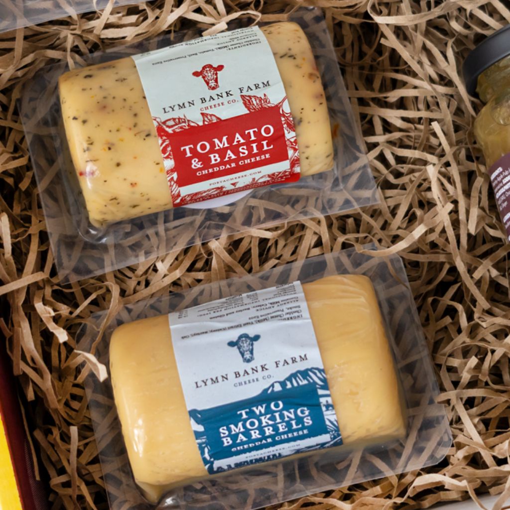 Tomato & Basil Cheddar and Two Smoking Barrels Cheddar packed in a cheese gift box with shredded paper.
