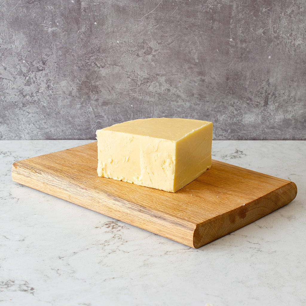 Chuckling Cheese Vintage Cheddar 1/4 Wheel on a wooden cheeseboard against a grey background