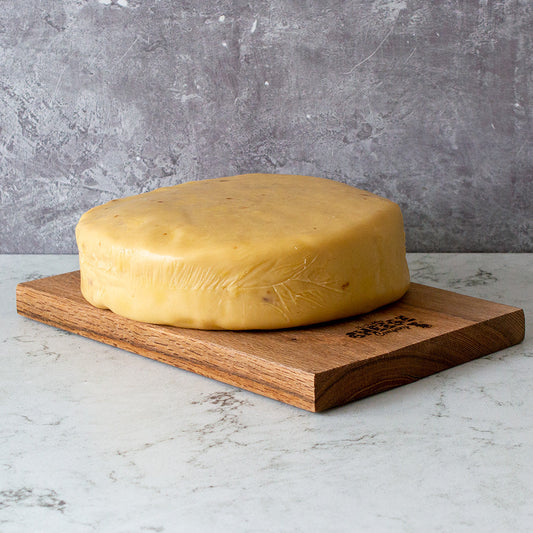 Large block of cheddar cheese on a wooden board against a grey background