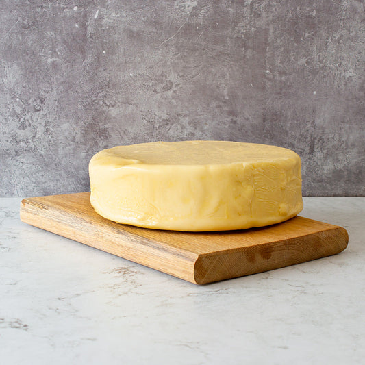 Wheel of mature cheddar cheese on a wooden board against a grey background.