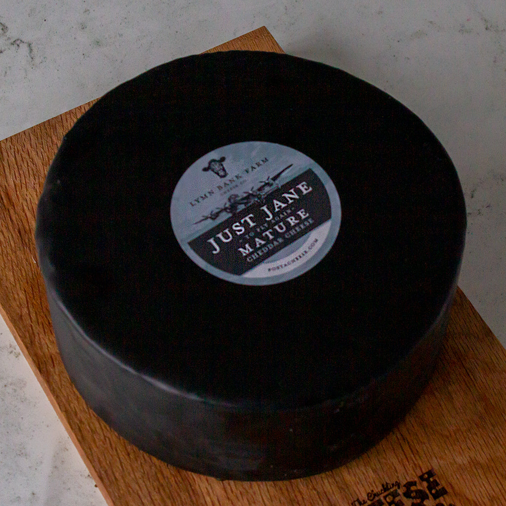 Large black wax-coated Just Jane Mature cheese wheel on a wooden board