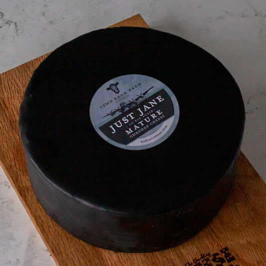 Large black wax-coated Just Jane Mature cheese wheel on a wooden board