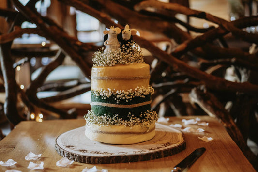 Four-tier cheese wheel wedding cake decorated with white flowers on a rustic wooden stand.