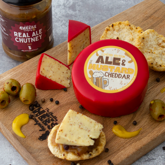 Chuckling Cheese Ale & Mustard Cheddar truckle with Real Ale Chutney, crackers, olives and mustard on a wooden board