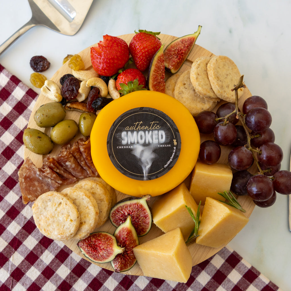 Authentic Smoked Cheddar cheese truckle on a grazing board with crackers, grapes, figs, strawberries, olives, nuts and sliced cheese.