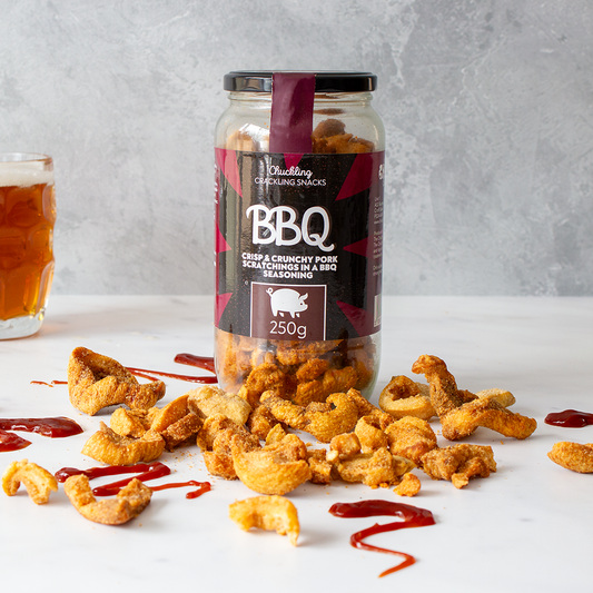 Chuckling Cheese BBQ pork scratchings jar with crispy pieces, sauce and beer on a grey background