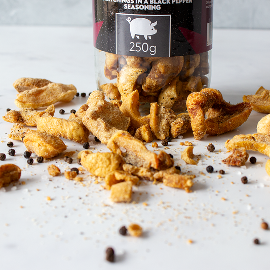 Chuckling Cheese Black Pepper pork scratchings jar with crispy pieces and scattered peppercorns