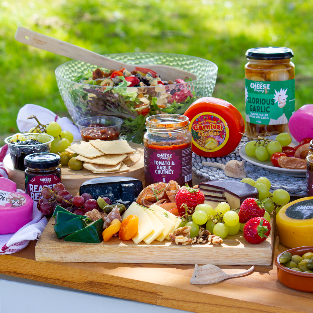 Outdoor Chuckling Cheese picnic spread with cheese truckles, chutneys, pickled onions, crackers, strawberries, grapes and salad