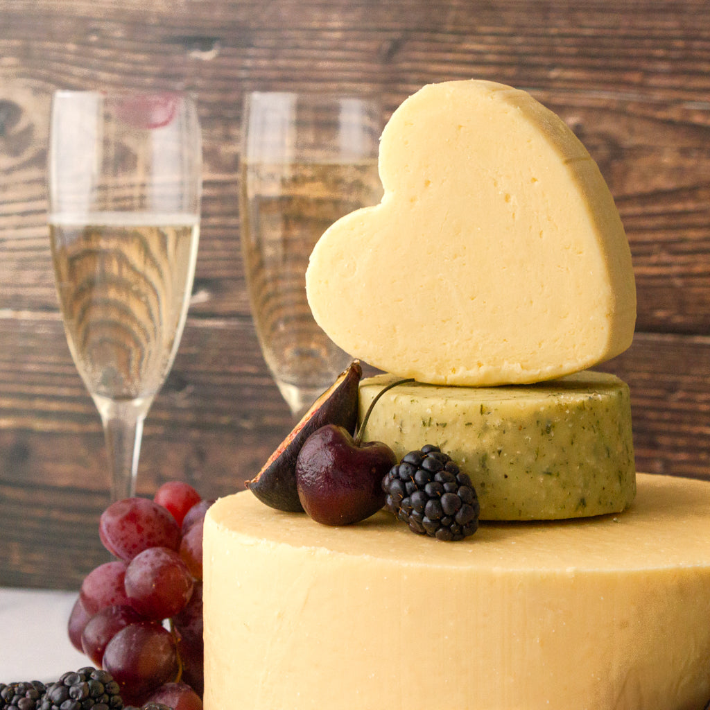 Wedding cheese cake with stacked cheese wheels, topped with a heart-shaped cheese and decorated with grapes and blackberries.