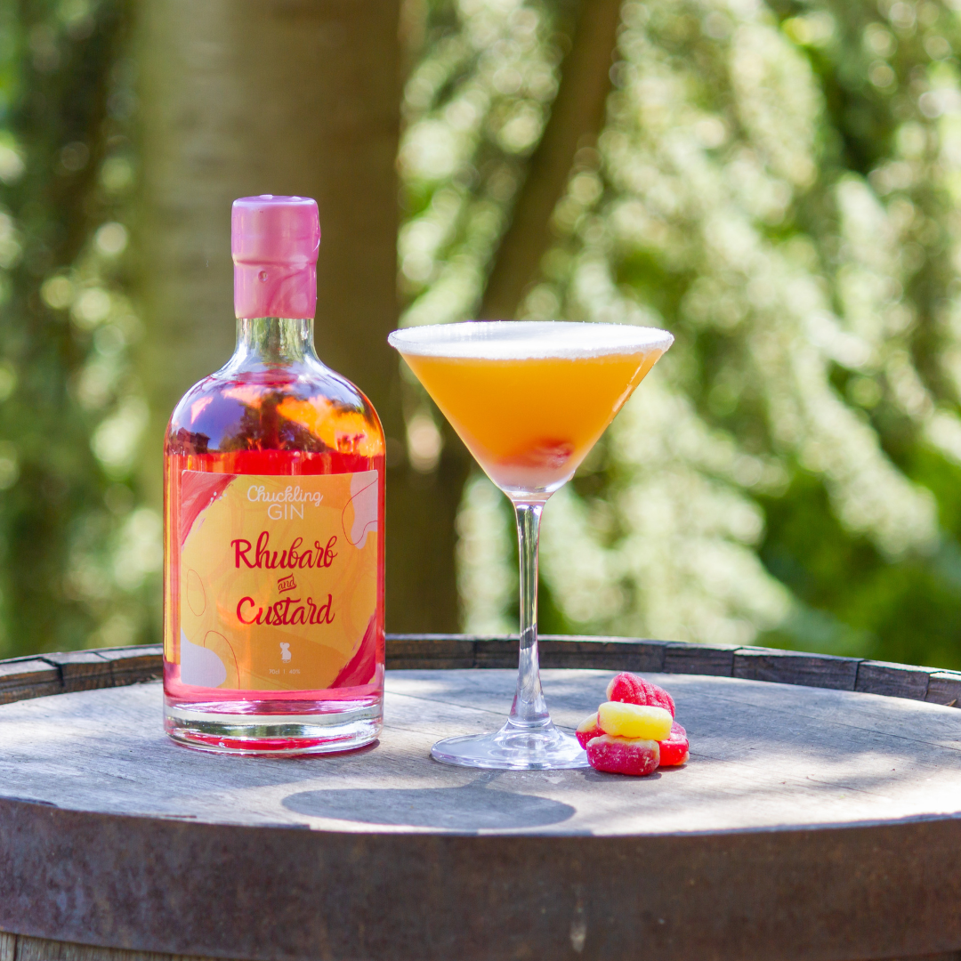 Chuckling Cheese Rhubarb & Custard Gin with cocktail glass and sweets on a wooden barrel