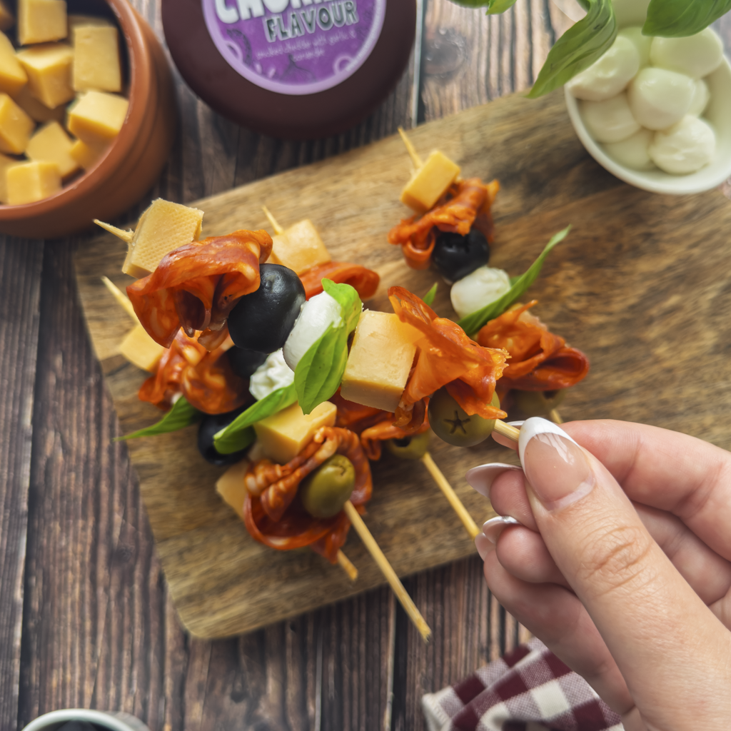 Cheese skewers with cheddar, cured meat, olives, mozzarella and basil on a wooden serving board.