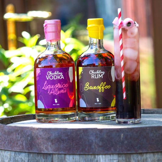 Liquorice Allsorts Vodka and Banoffee Rum bottles beside a tall layered cocktail on a wooden barrel
