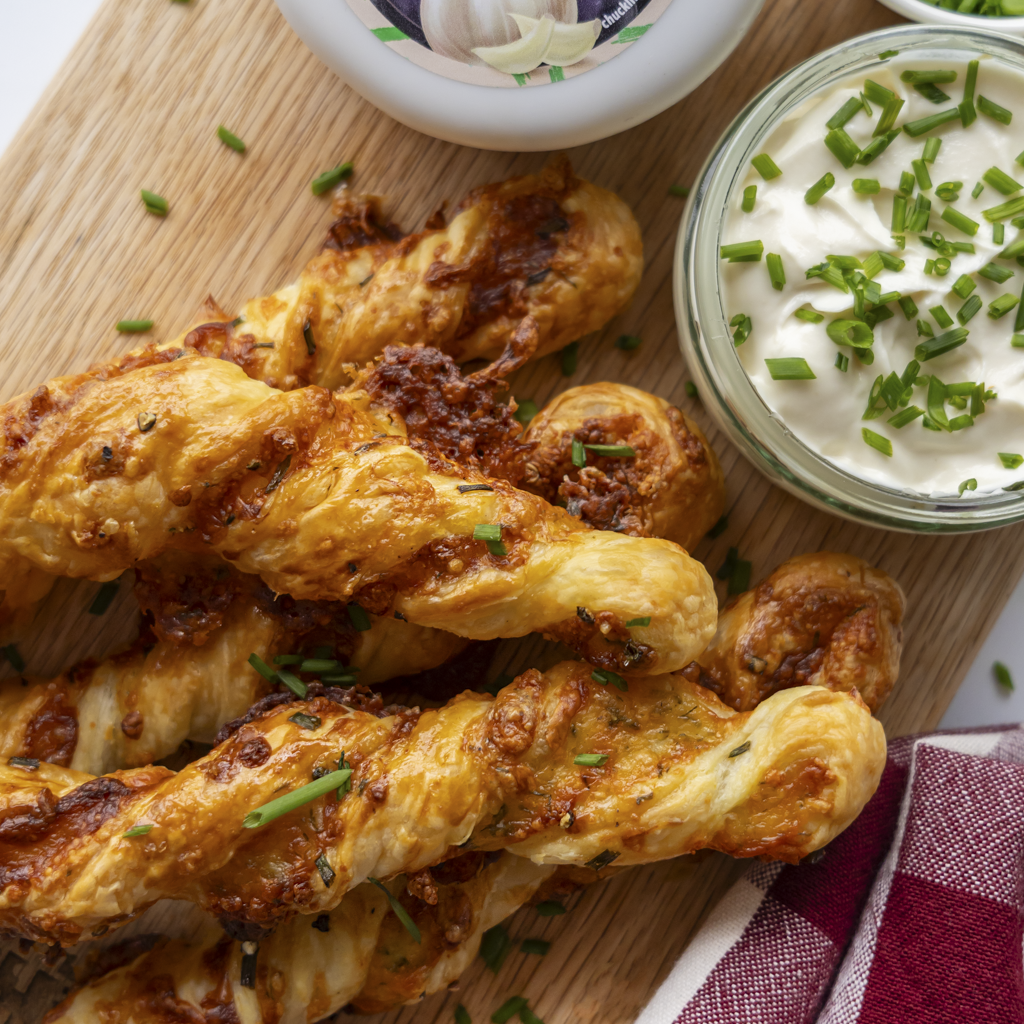 Homemade garlic and chive cheese twists with creamy sauce on a wooden cutting board