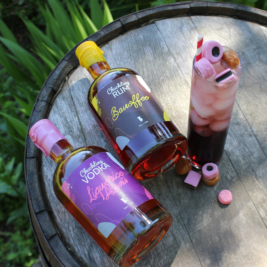 Chuckling Cheese Liquorice Allsorts vodka with pink cocktail, sweets and bottles on a wooden barrel