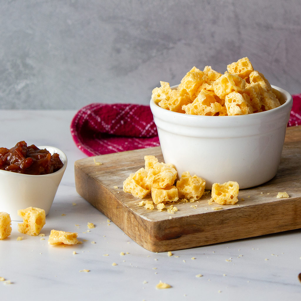 Chuckling Cheese crunchy cheese snack pieces in a white bowl with chutney on a wooden board
