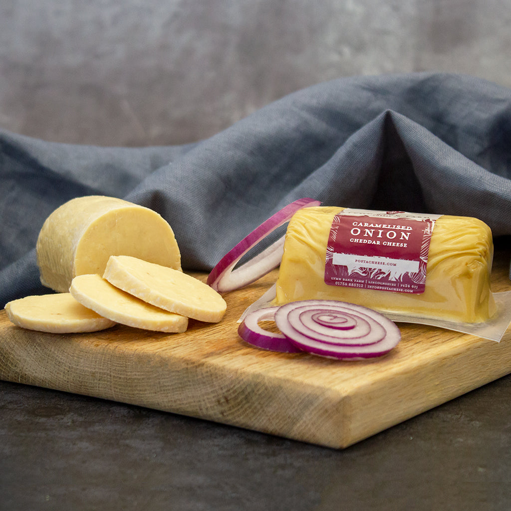 Chuckling Cheese Caramelised Onion Cheddar Barrel with onion slices and cheese on a board