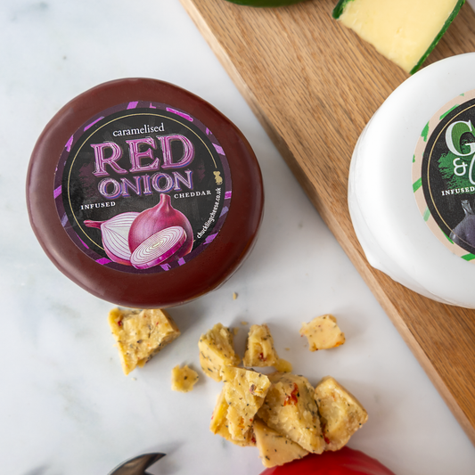 Red Onion Cheddar and Garlic & Chive cheese truckles with pieces of cheese and crackers on a serving board.