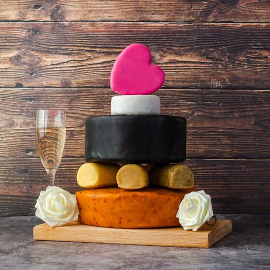 Tiered cheese wedding cake topped with a pink heart and decorated with white roses.
