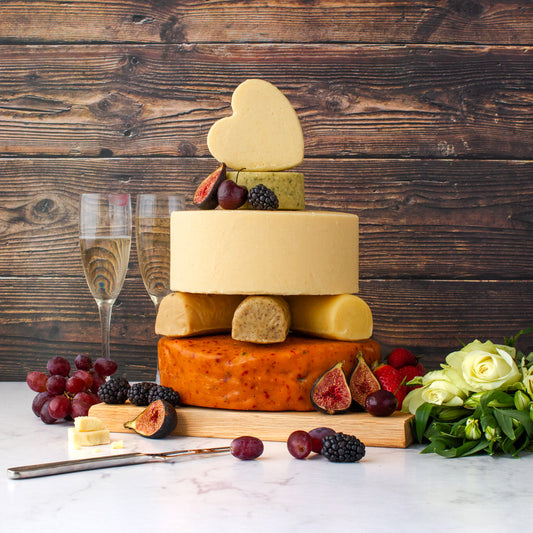 Celebration cheese cake made with stacked cheese wheels, topped with a heart-shaped cheese and decorated with fruit and flowers.