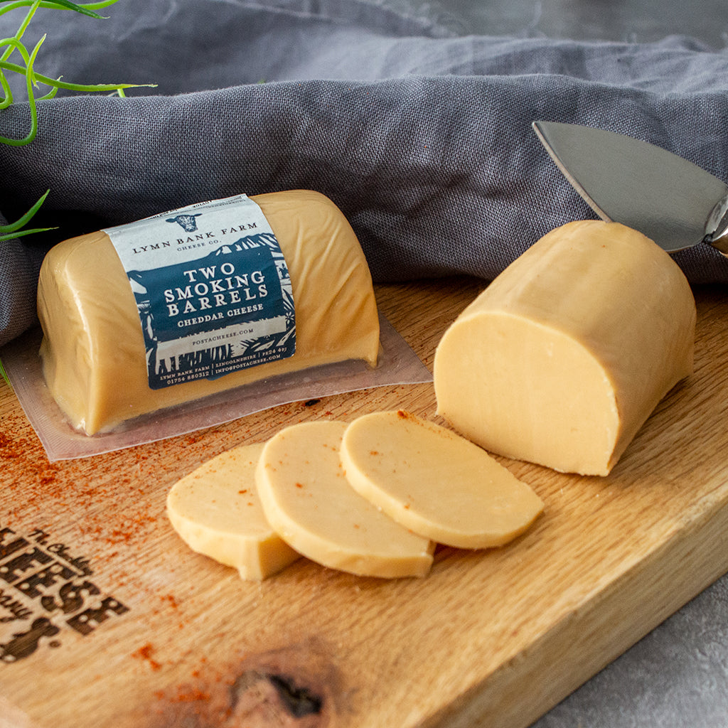 Chuckling Cheese Two Smoking Barrels cheddar with sliced cheese and a cheese knife on a wooden board