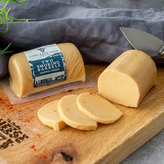 Chuckling Cheese Two Smoking Barrels cheddar with sliced cheese and a cheese knife on a wooden board