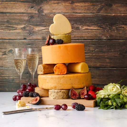 Birthday cheese cake tower made with stacked cheese wheels, topped with a heart-shaped cheese and served with fruit, flowers and sparkling wine.