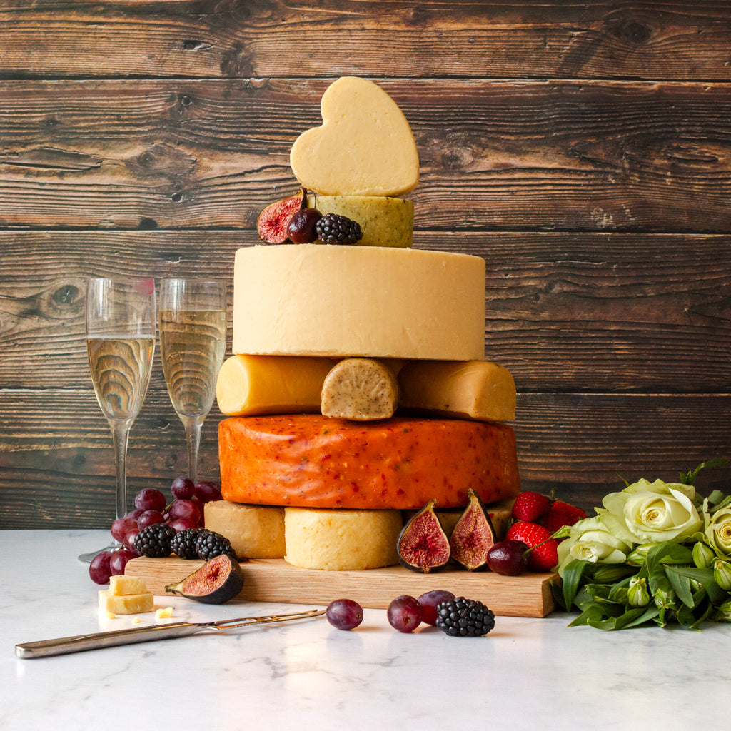 Chuckling Cheese celebration cheese cake with stacked cheese wheels, heart topper, fruit and champagne