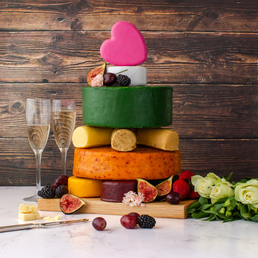 Cheese wheel wedding cake decorated with fruit, flowers and a heart topper