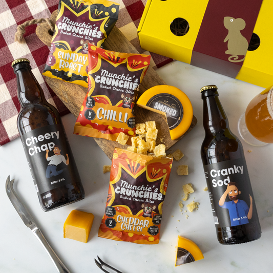 A cheese truckle, cheese bake bites, and 2 beer bottles on a white table surface.