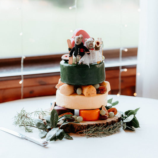 Three-tier celebration cheese cake decorated with greenery, fruit and a personalised wedding topper
