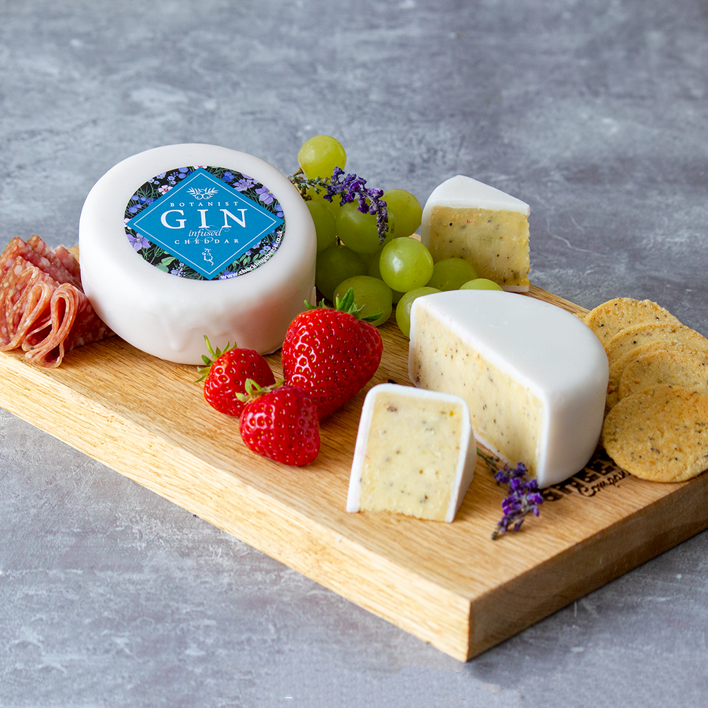 Chuckling Cheese Botanist Gin & Tonic Cheddar Truckle on a wooden board with strawberries and green grapes.