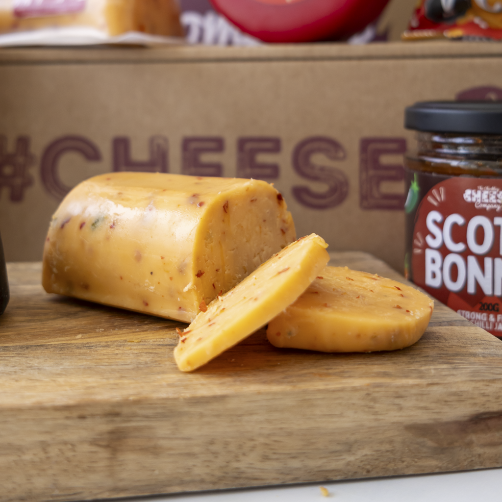 Sliced Hot & Spicy Cheddar Barrel on wooden board with Scotch Bonnet jam
