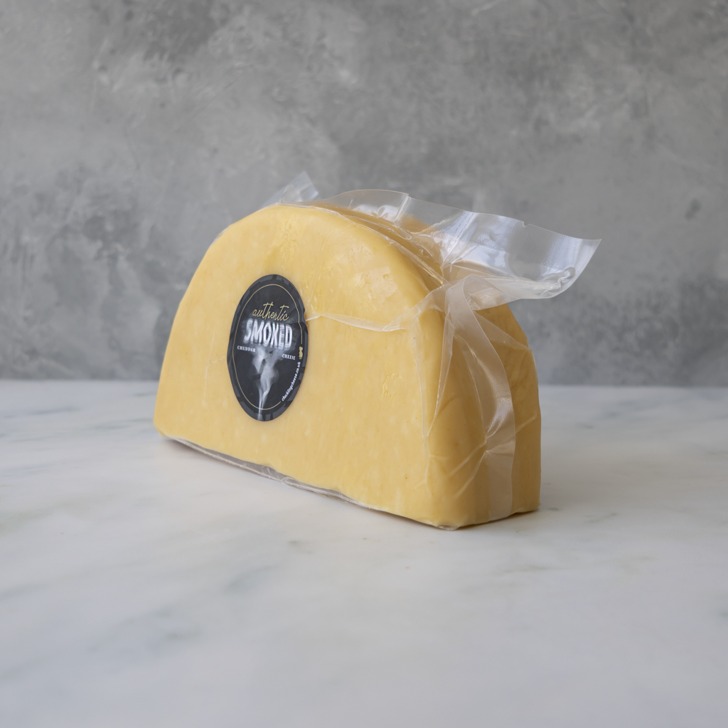 Apple Smoked Cheddar 1/2 Wheel wrapped in plastic with a label on a marble surface