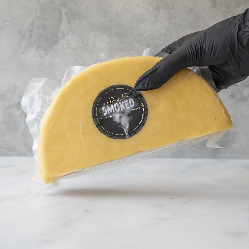 Apple Smoked Cheddar 1/2 Wheel with a black label held by a gloved hand against a gray background