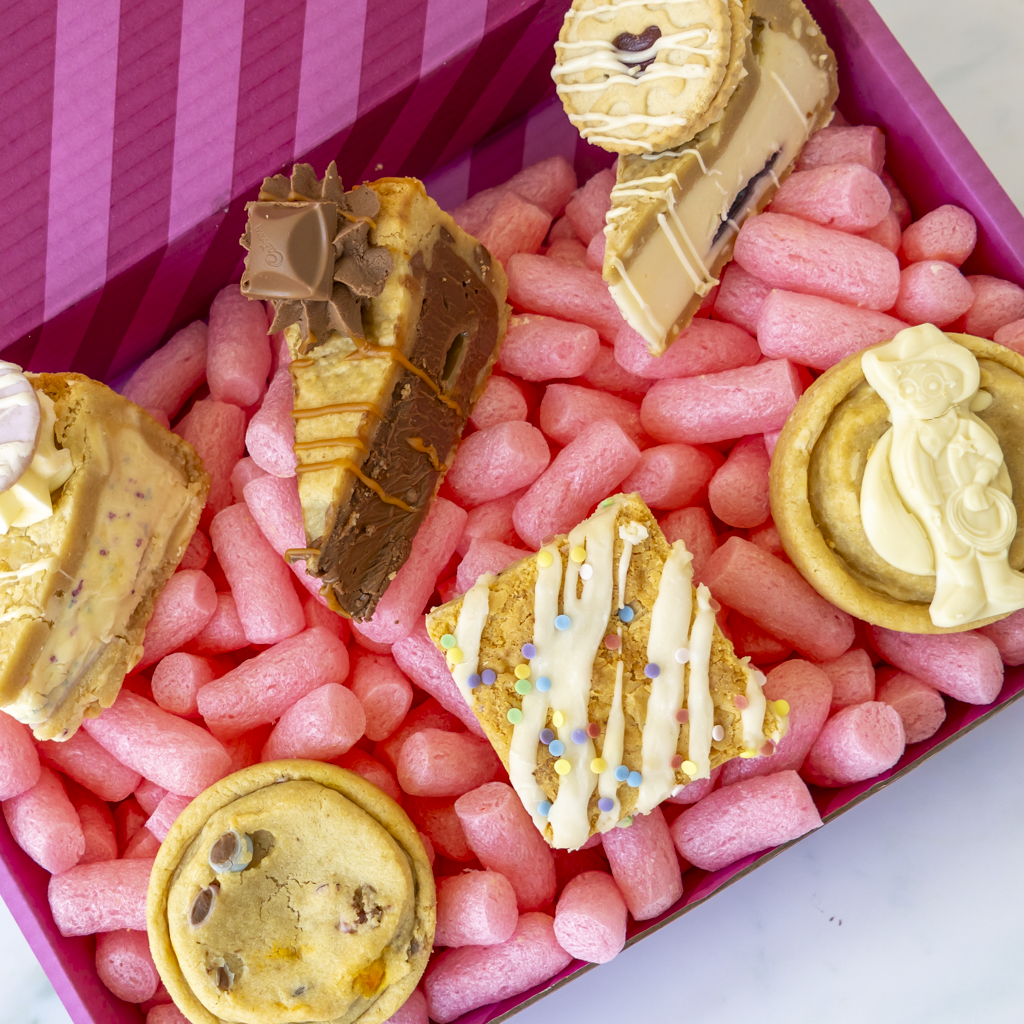 A boxed assortment of assorted cookies and chocolate treats arranged in pink cookie box.