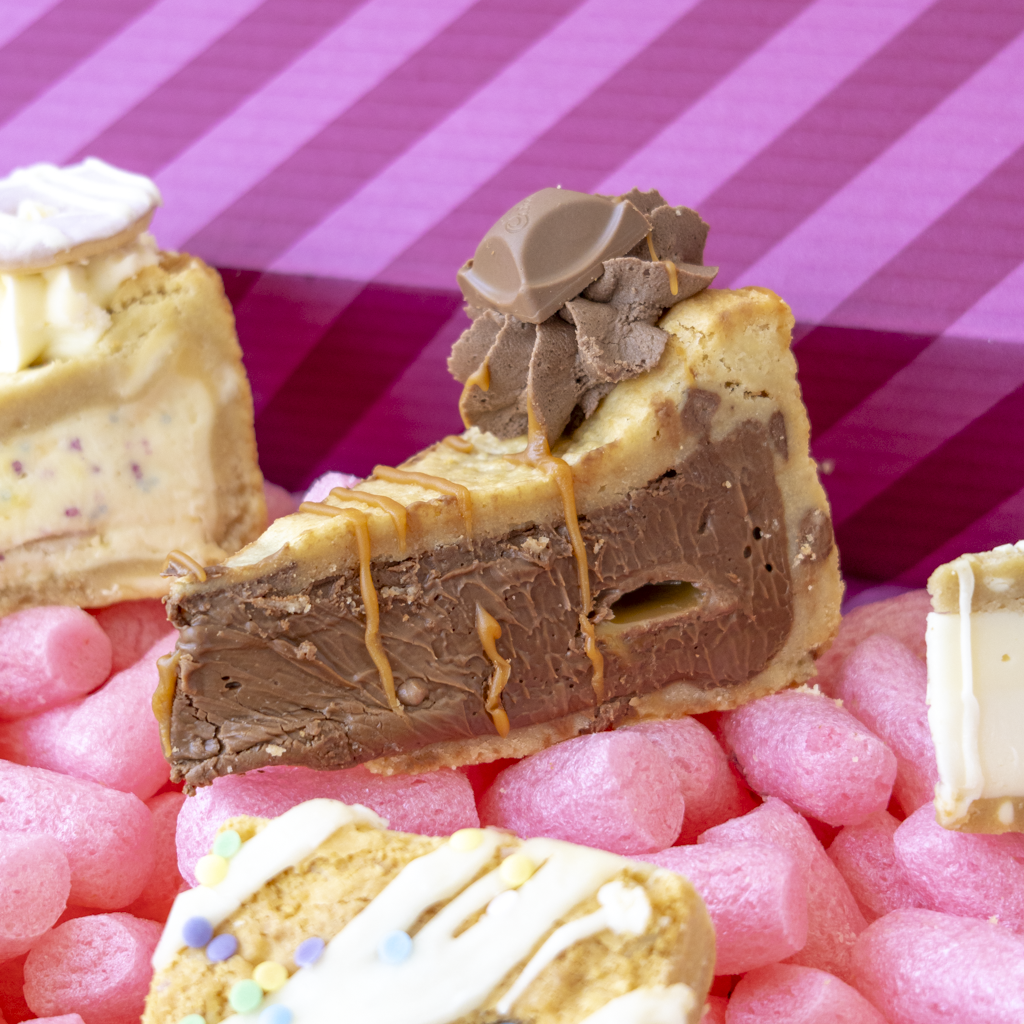 A close-up of assorted chocolate and cream dessert slices against a pink striped background.