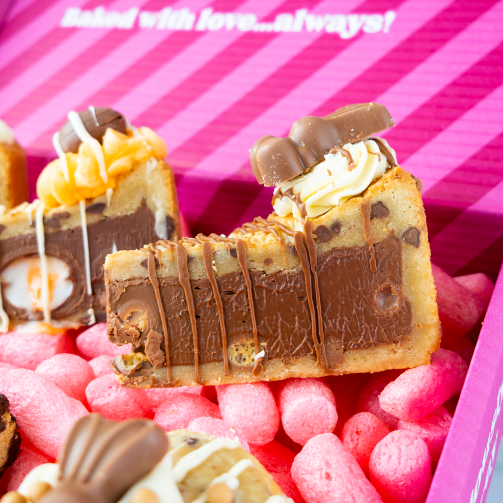 Decorative slice of cookie with chocolate and caramel elements on a pink striped background