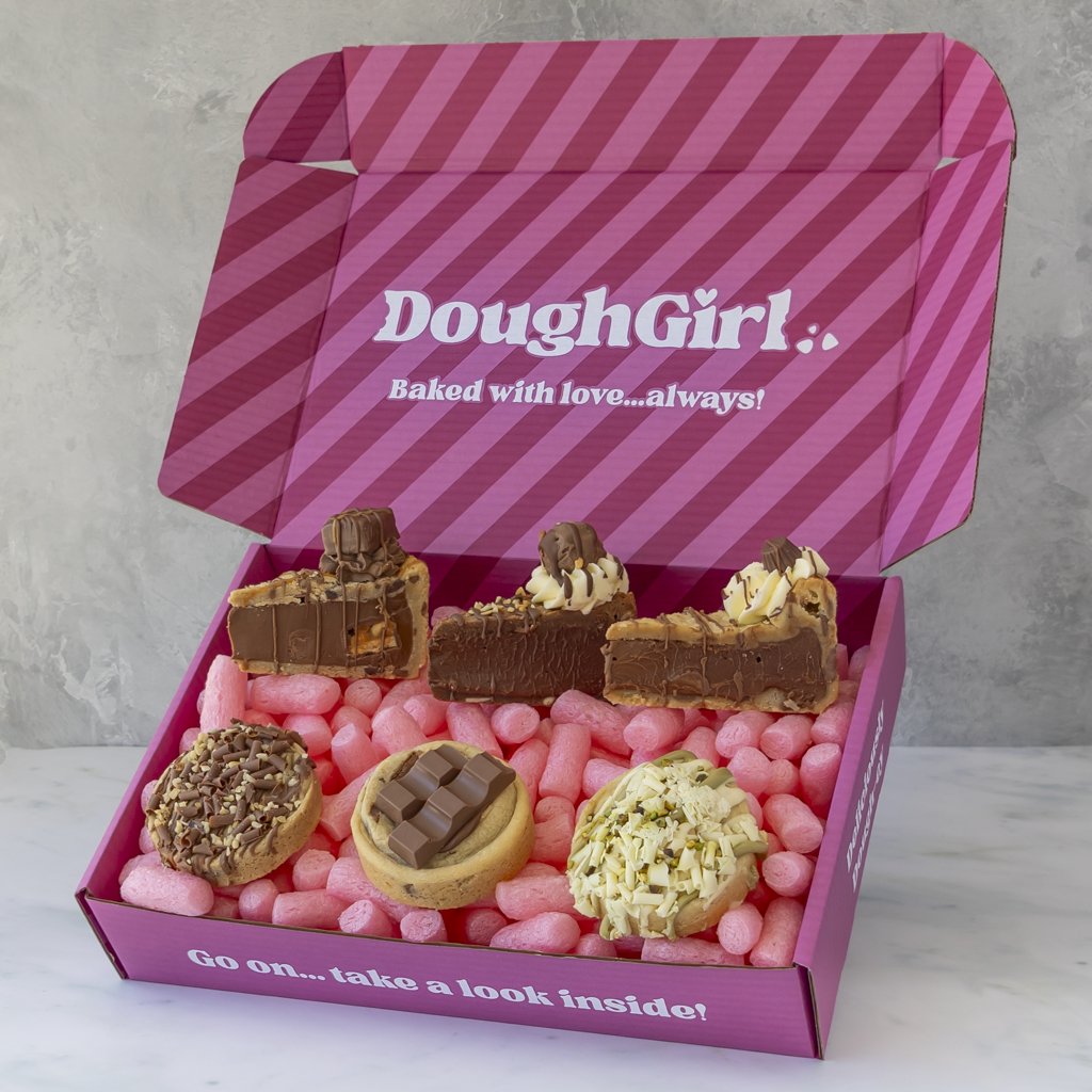 An open pink gift box with diagonal pink stripes and the brand name 'DoughGirl' printed on the inside lid. The box is filled with assorted baked goods, including chocolate cookie pie slices, a chocolate-covered cookie, a nut-topped pastry, and a cream-topped pastry.
