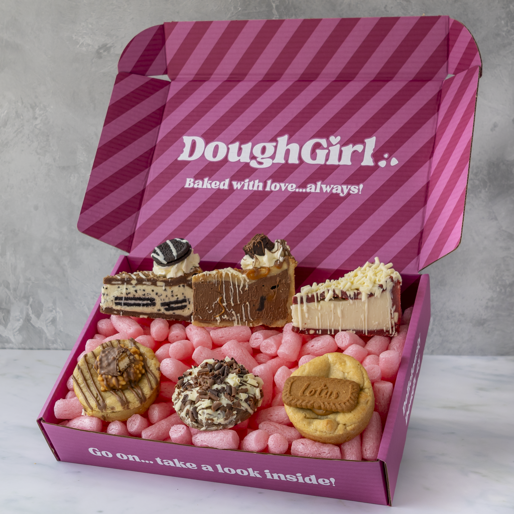A pink striped DoughGirl baking gift box filled with assorted cookies, cookies pie slices, and pink gummy bears, shown on a light gray background.