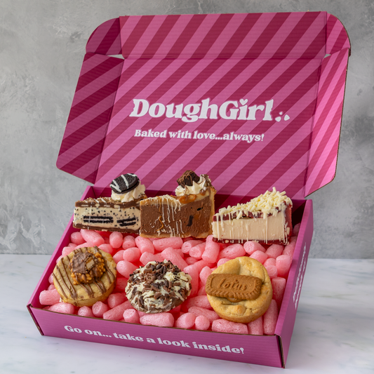 A pink striped DoughGirl baking gift box filled with assorted cookies, cookies pie slices, and pink gummy bears, shown on a light gray background.