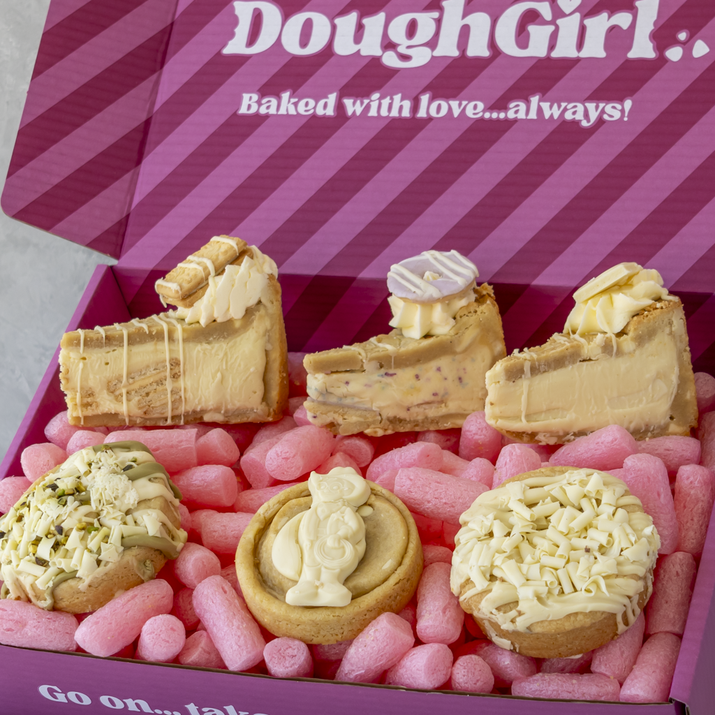 A boxed assortment of baked desserts displayed in a pink gift box. The box lid reads 'DoughGirl.