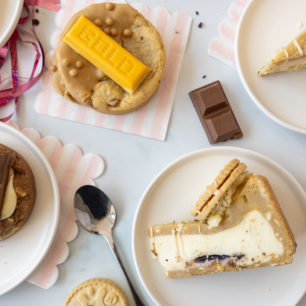 A styled flat-lay of dessert cookies and cookie pie slices on white plates, with a chocolate bar placed on a napkin.