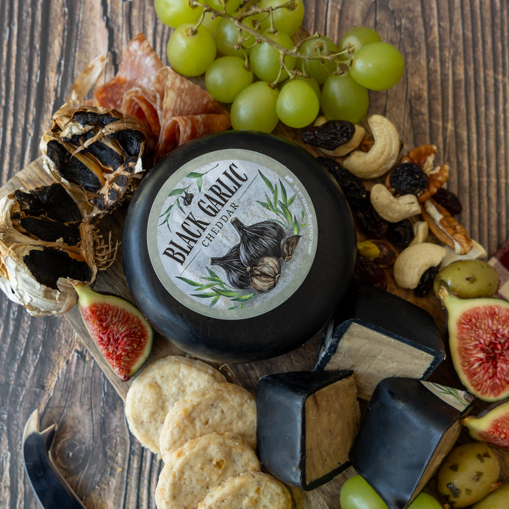 Black Garlic Cheddar Truckle close-up with crackers, grapes, black garlic and cheeseboard accompaniments