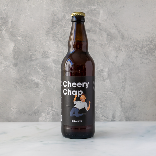 A dark brown glass beer bottle with a black label reading 'Cheery Chap' and a small illustrated figure, standing on a white marble surface against a textured gray concrete wall.