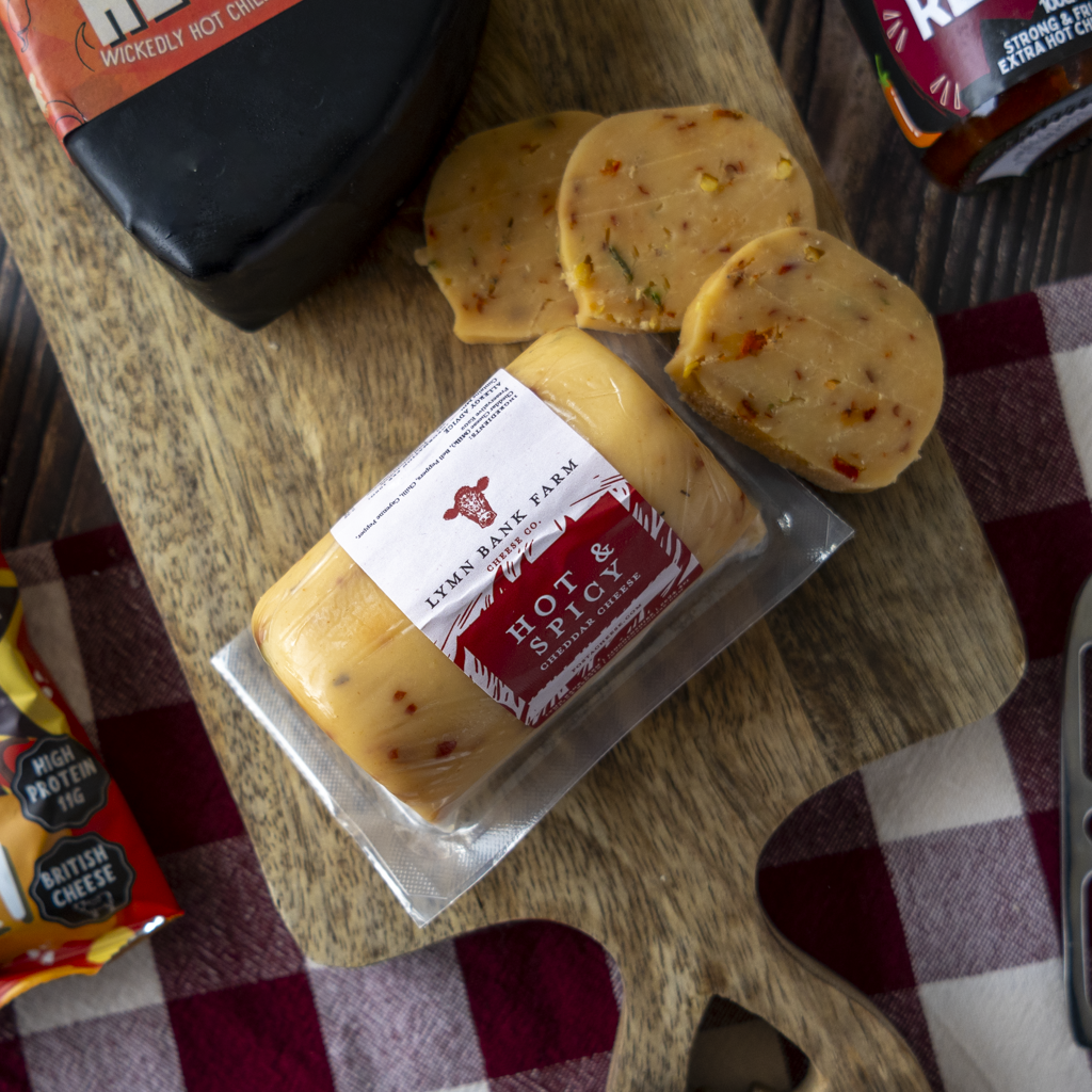 Hot & Spicy Cheddar with crackers and Chilli Lovers Gift Box treats on a wooden board.