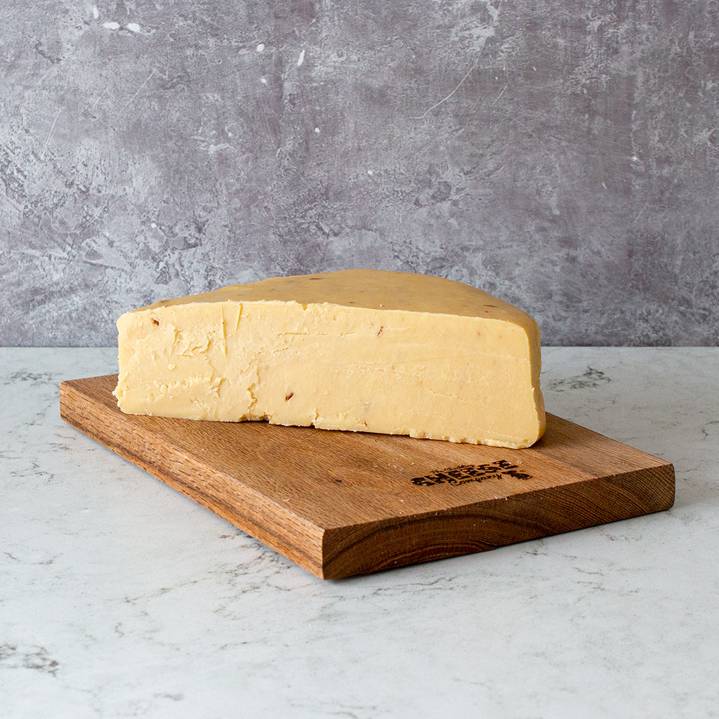Chuckling Cheese Caramelised Red Onion Cheddar 1/2 Wheel (1.1kg) on a wooden cheeseboard against grey backgound