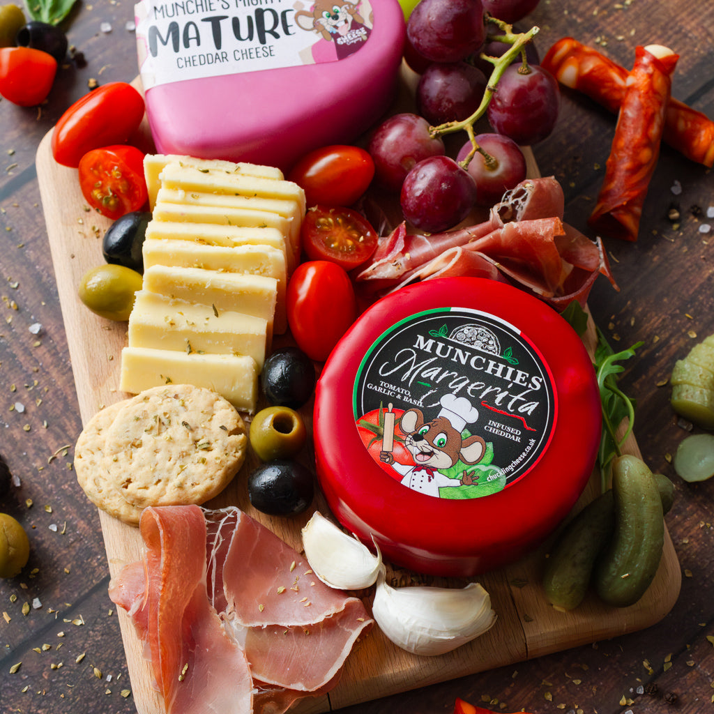 Close-up of a cheese grazing board with cheddar truckles, crackers, cured meat, grapes and olives.