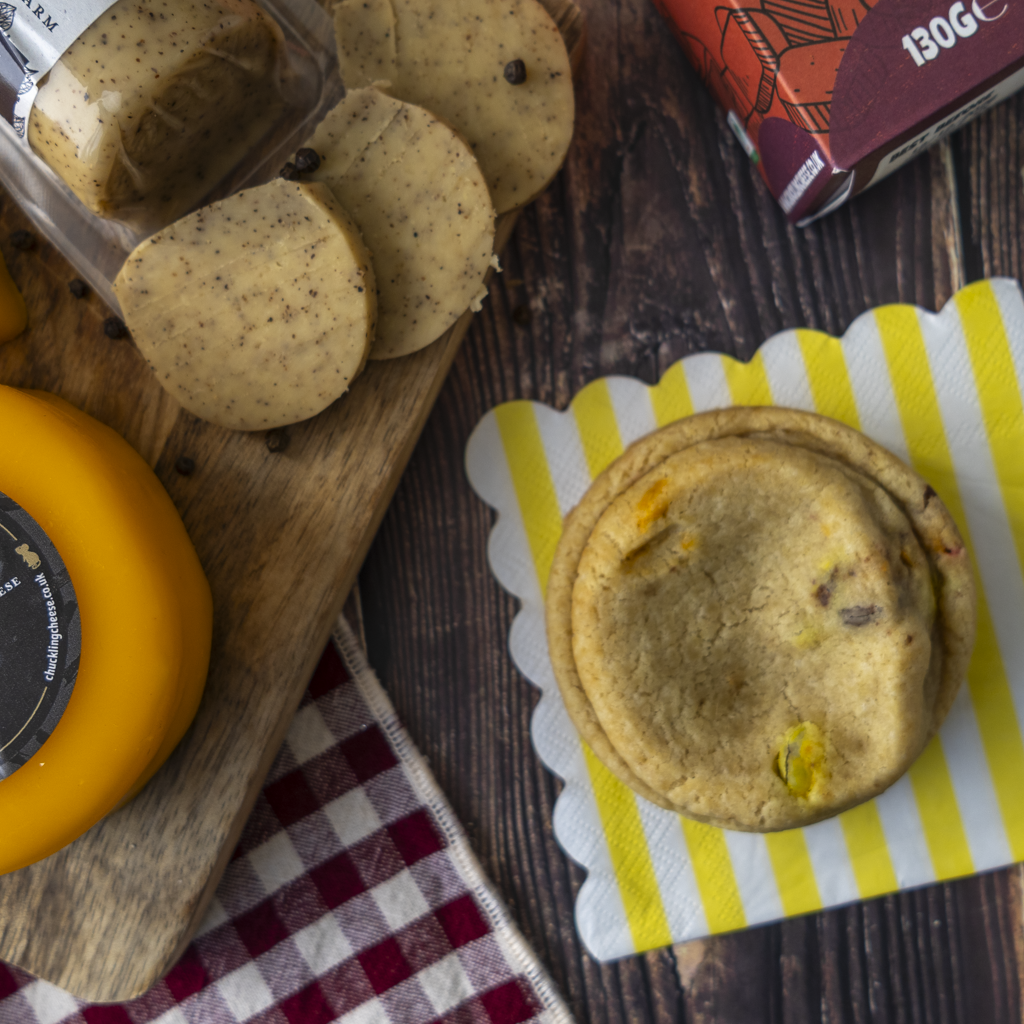 A styled food product shot featuring a rainbow cookie with a visible yellow cheese truckle, stacked on a yellow-and-white striped paper napkin.