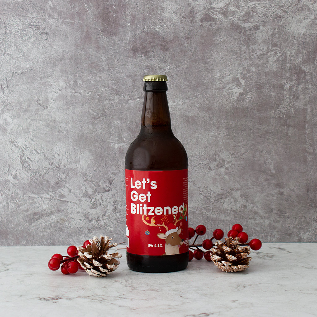 “Let’s Get Blitzened” Christmas beer bottle styled with pine cones and red berries.
